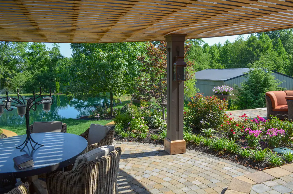 Covered seating area with paver patio, wood ceiling, columns, planting beds, lawn view, and outdoor dining furniture.